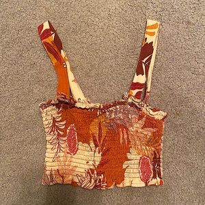 A ruched crop top that has a tropical floral pattern and has adjustable straps.
